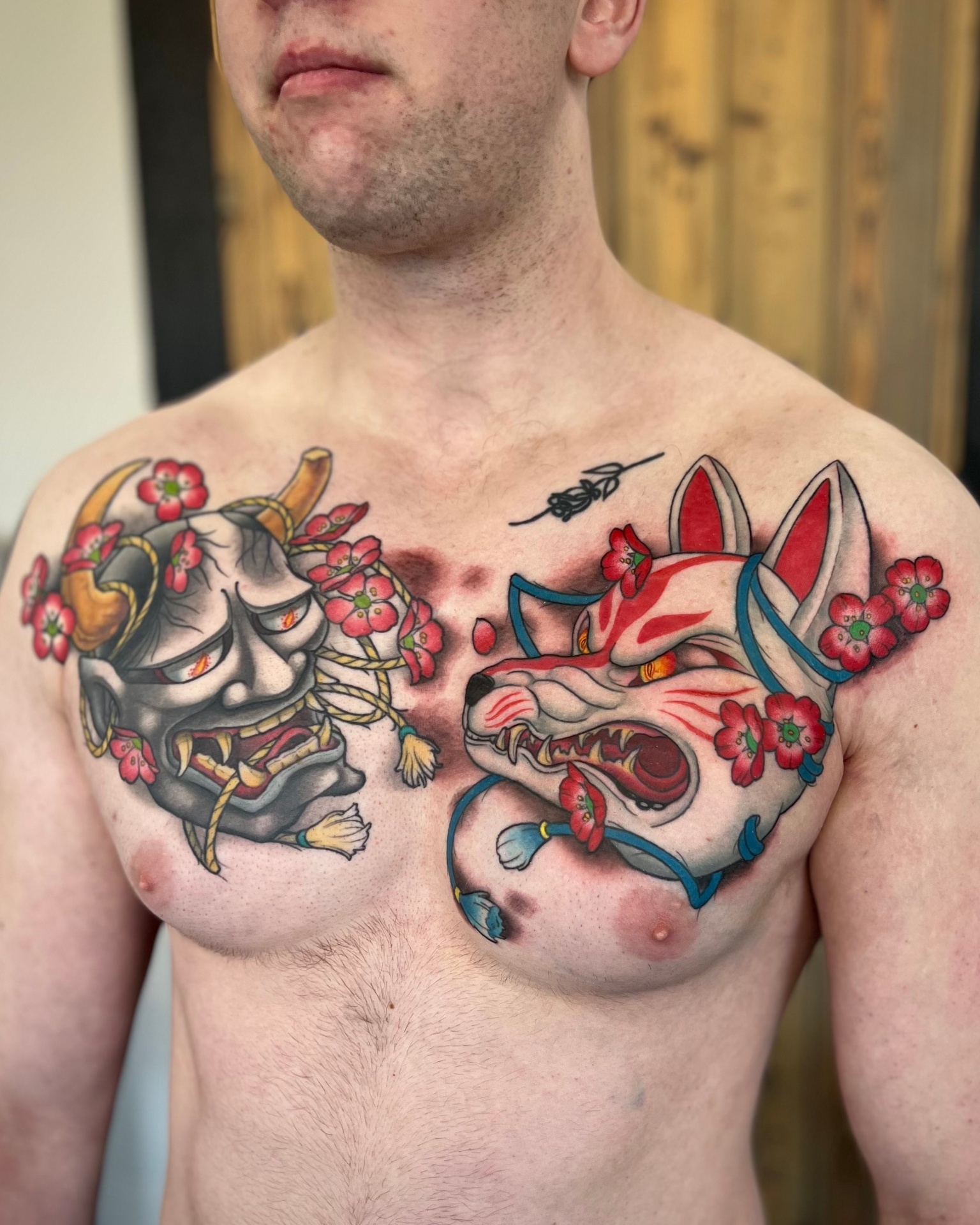 Bold chest tattoo with oni mask and fox mask by Crimson Empire Tattoo