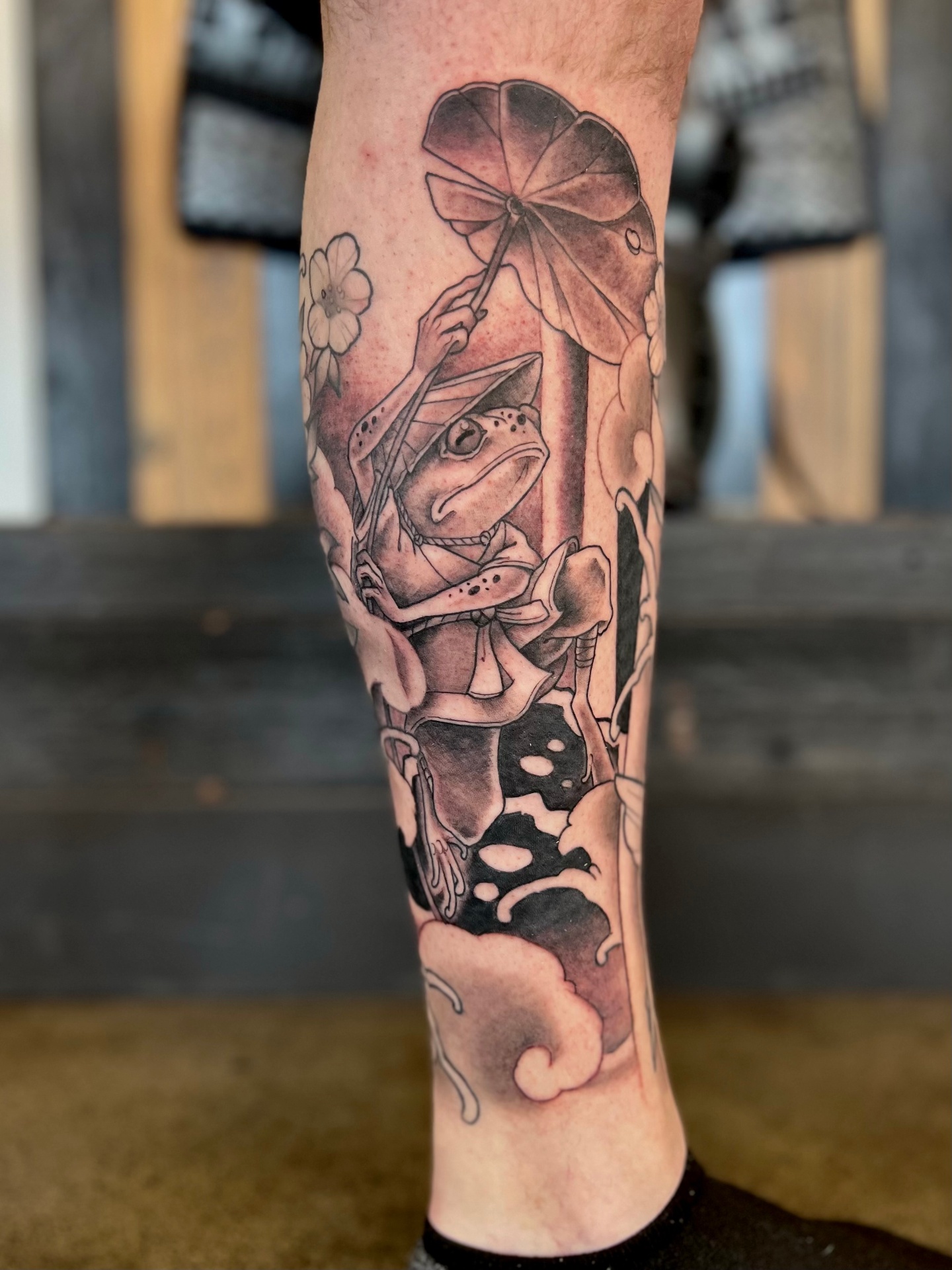 Black-and-grey frog tattoo holding a leaf umbrella